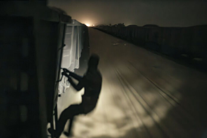 A Young Mauritanian Man Hangs On The Side Of The Train While It Rides Through The Desert At Night