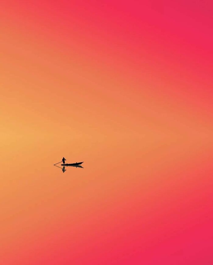 A minimalist surreal photo of a lone figure on a boat, with a vibrant orange and pink gradient sky.