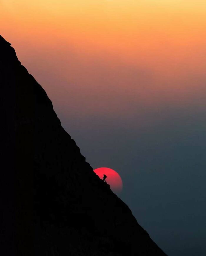 Climber silhouetted on a mountain at sunset, capturing minimalism and mystery.