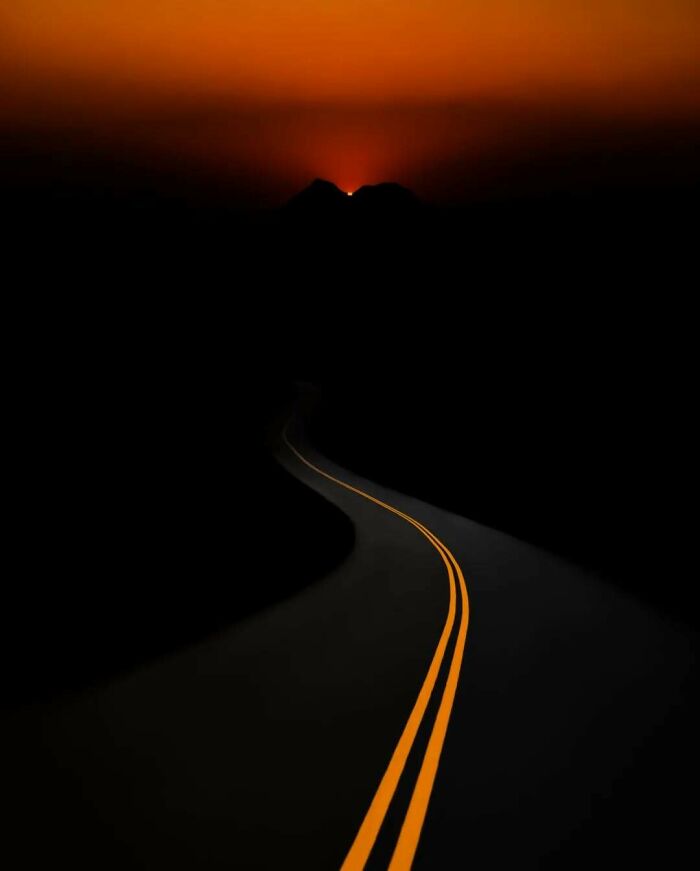 A surreal road at night with yellow lines leading to a glowing horizon.