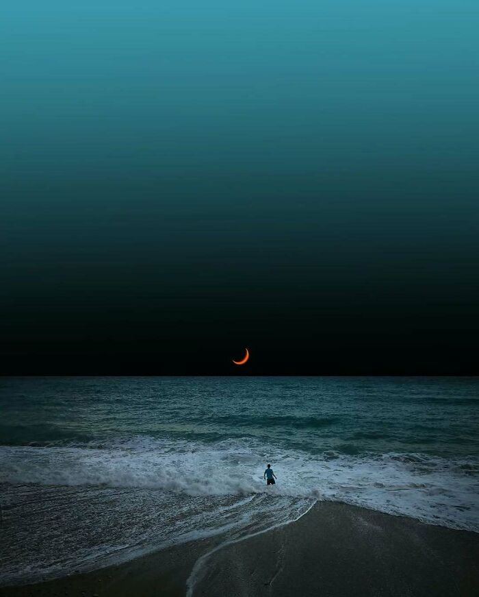 A person stands at the ocean's edge under a crescent moon, reflecting minimalism and mystery.