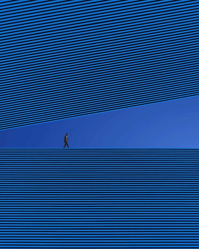 A person walking on blue and black striped surreal landscape, showcasing minimalism and mystery.