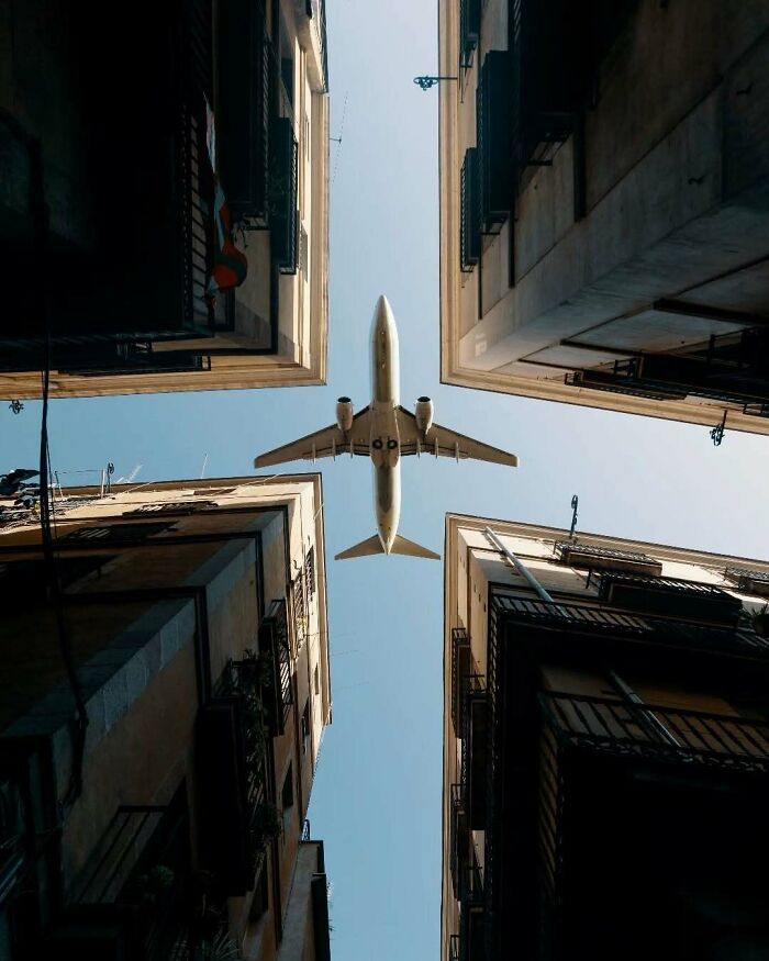 Surreal photo of an airplane flying above between two tall buildings, capturing minimalism and mystery.