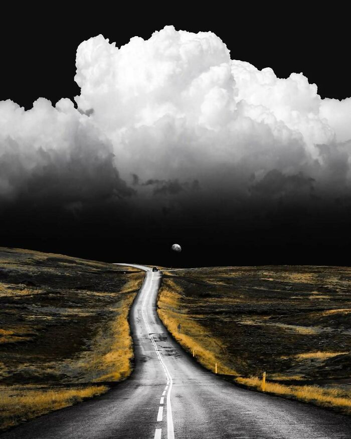 A surreal, minimalist road under dramatic clouds with a mysterious moon by Benjamin Wolf.