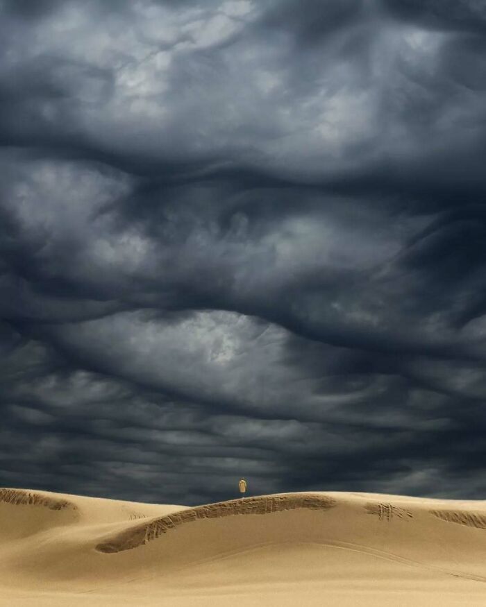 Surreal photo by Benjamin Wolf featuring a lone figure in a vast desert under a dramatic, cloudy sky.