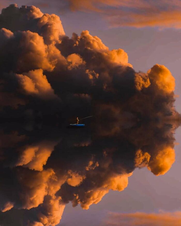 Surreal photo of a person fishing on a small boat against dramatic, cloud-filled sky.