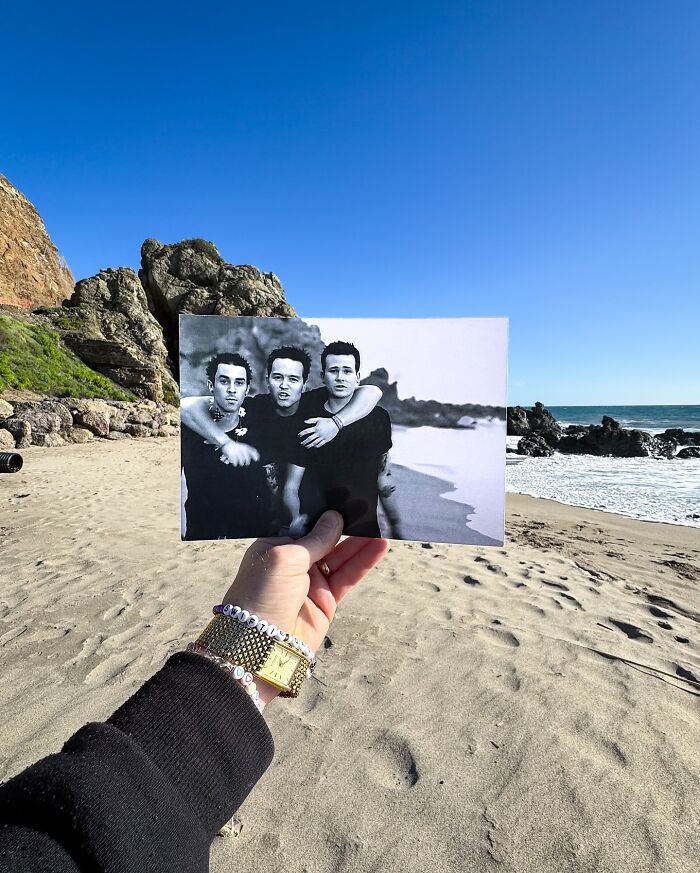 A person holds a black and white photo at a beach location, capturing iconic scenery from the past.