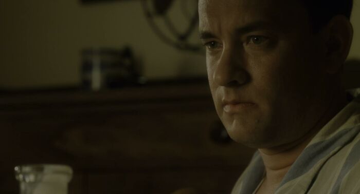 A 90s celebrity in a dimly lit room, wearing a robe, against a blurred wooden background.