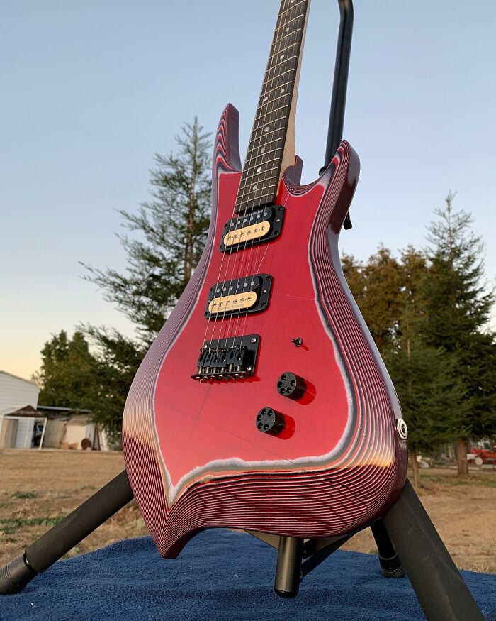 Stunning guitar made from unexpected materials with a unique layered design, displayed outdoors on a stand.