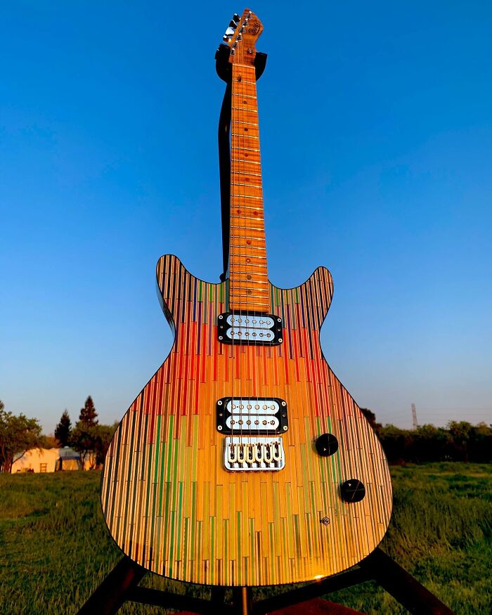 Stunning guitar made by an artist from unexpected materials, featuring a colorful, striped design against a clear blue sky.