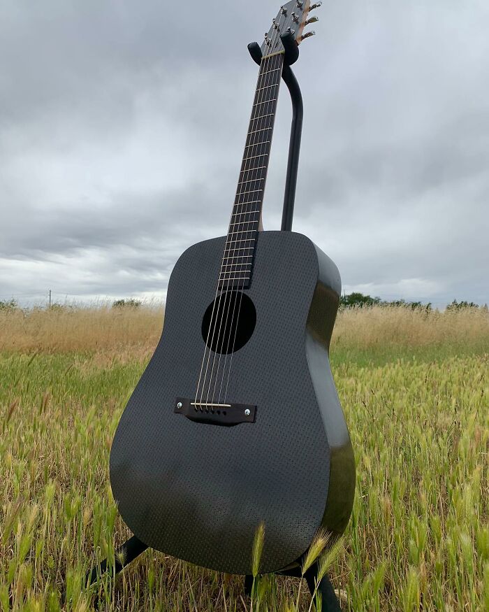 Stunning guitar made from unexpected materials, displayed in a grassy field under cloudy skies.