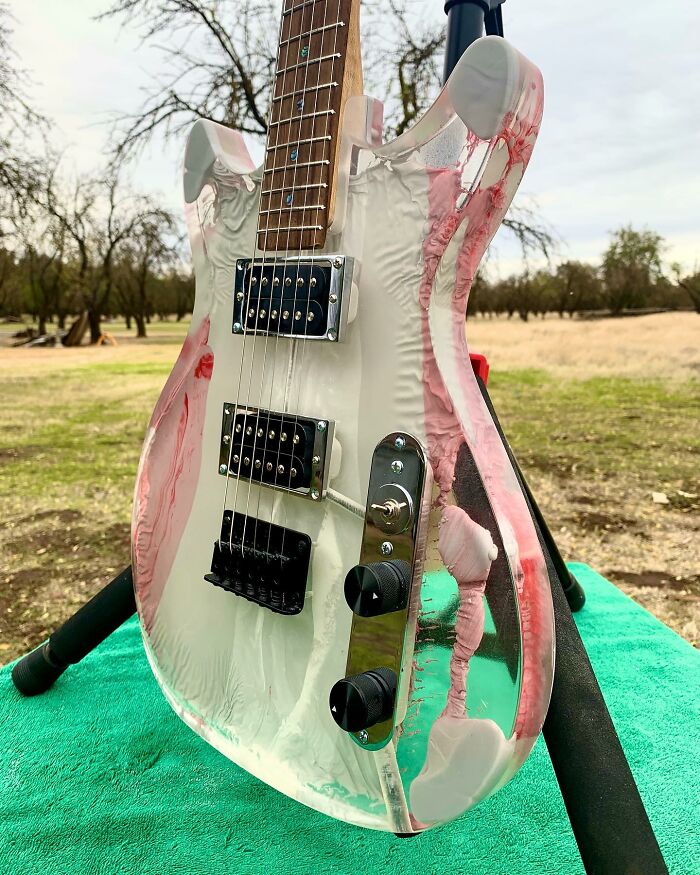 Guitar built from unexpected materials, featuring a translucent body with pink and white swirls, displayed outdoors.