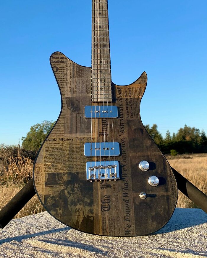 Guitar made from newspaper material, showcasing unique artistry against a clear blue sky background.