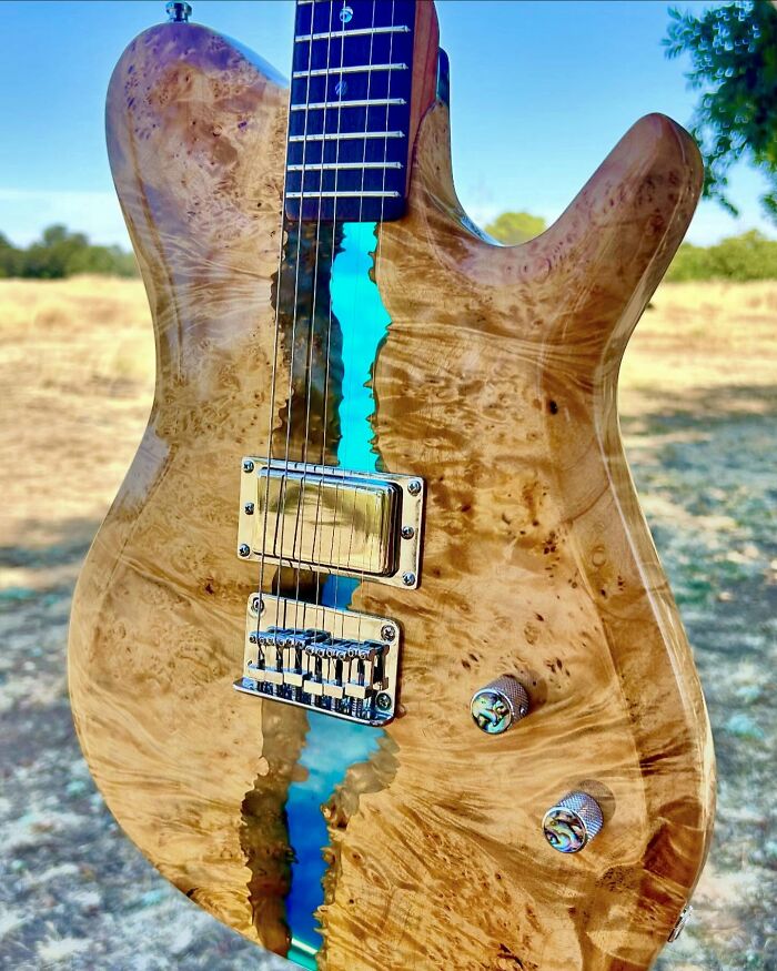 Unique guitar crafted from wood and blue resin, showcasing stunning design and unexpected materials in an outdoor setting.