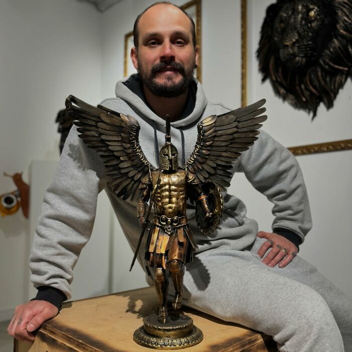 Artist with scrap metal sculpture of a warrior in an art studio, showcasing intricate details and craftsmanship.
