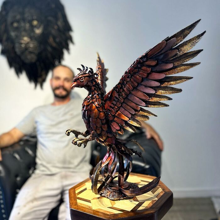 Sculptor with a detailed scrap metal phoenix on a wooden table.