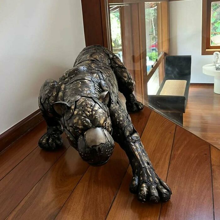 Scrap metal sculpture of a prowling panther on a wooden floor in a modern room.