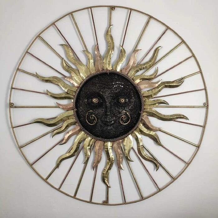 Scrap metal sculpture depicting a sun face with intricate metalwork, featuring golden and bronze colors.