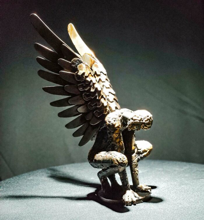 Sculpture of a crouching figure with wings, made from scrap metal, showcasing intricate detail and craftsmanship.