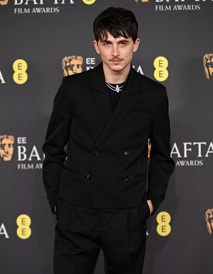 A person in a black suit at the BAFTA red carpet, showcasing daring outfits and trends.