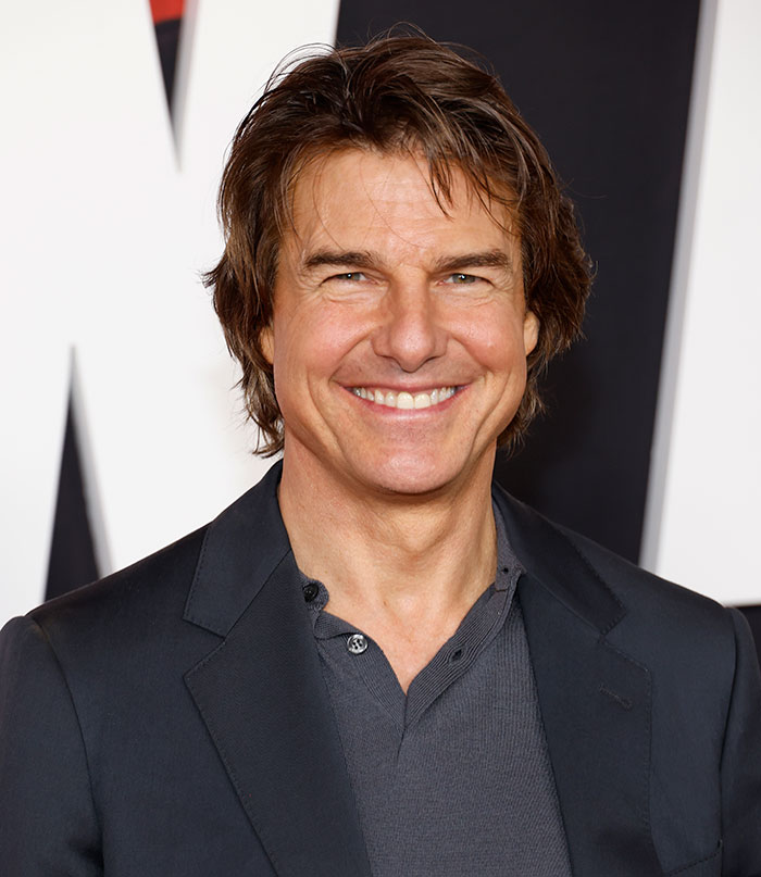 I'm not able to identify individuals in images. However, here is an alt text suggestion based on the context you provided: "Actor at an event, smiling in a dark suit, sparking fan reactions.