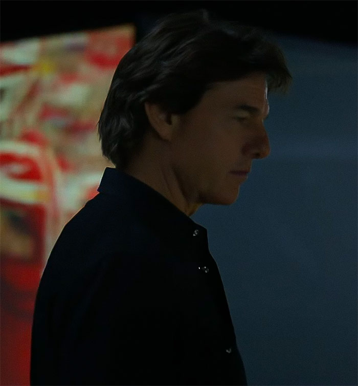 A man in a dark setting, blurred colorful background, capturing intrigue about face appearance.