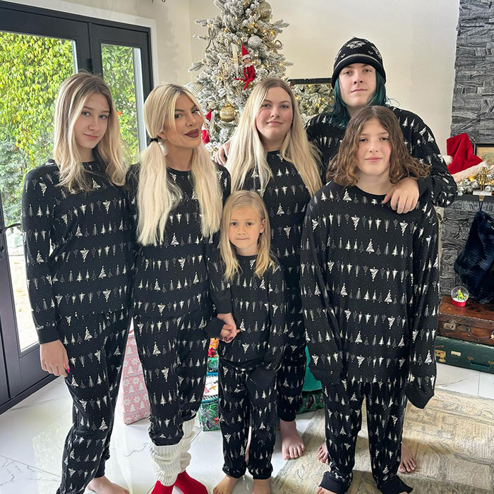 Family wearing matching pajamas in front of Christmas tree.