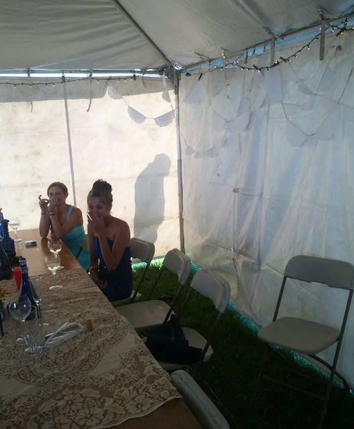 Guests looking surprised inside a wedding tent with empty chairs and a decorated table.