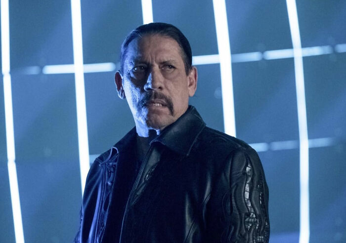 Man with a mustache in a leather jacket, standing in a dimly lit setting with blue light bars; today I learned facts theme.