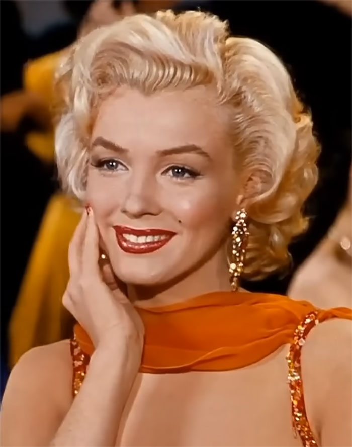Blonde woman in an orange dress smiling, embodying celebrity charm and style.