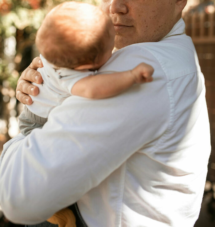 A person gently holding a baby outdoors, wearing a white shirt.