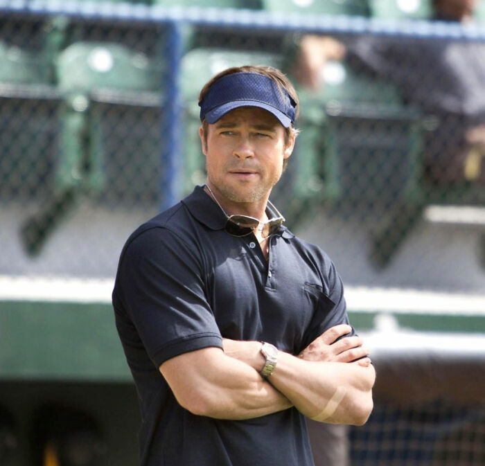 A celebrity in a navy polo and visor at a sports venue, reflecting on newfound insights.