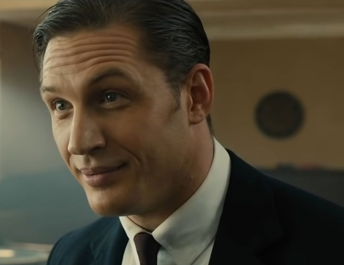 A man in a suit with slicked-back hair, representing challenging actors to work with, smirking slightly.