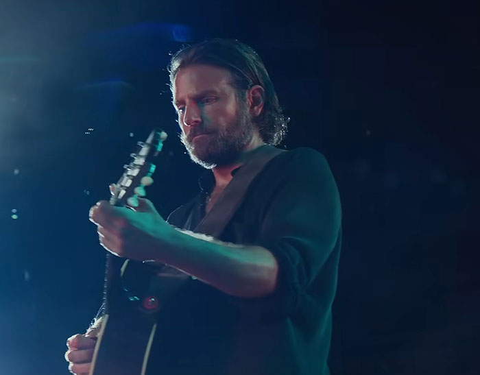 Actor playing guitar on stage under moody lighting, embodying intense emotion and focus in the performance.