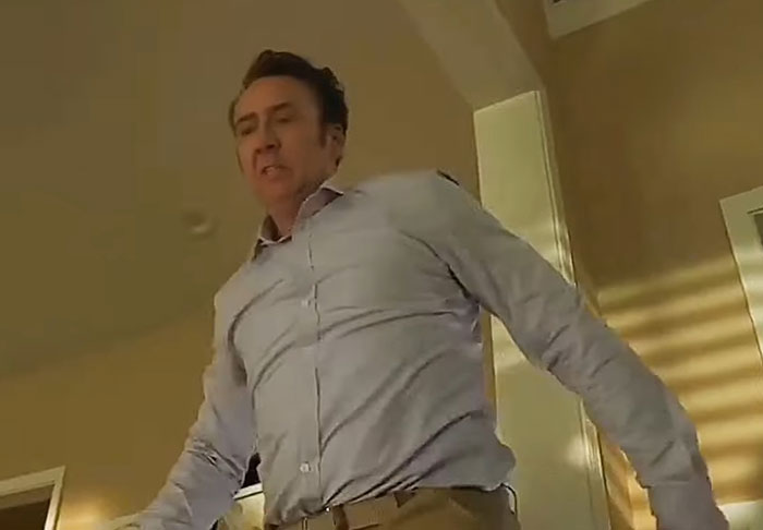 Actor in a tense scene, wearing a light shirt, in a brightly lit room.