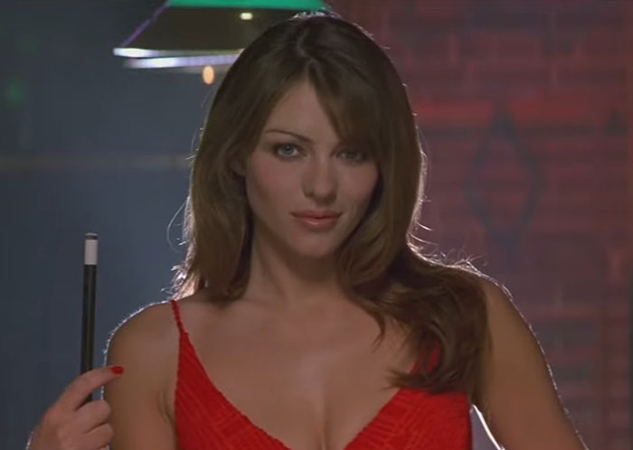 A woman in a red dress poses with a pool cue in a dimly lit room, related to actors challenging to work with.