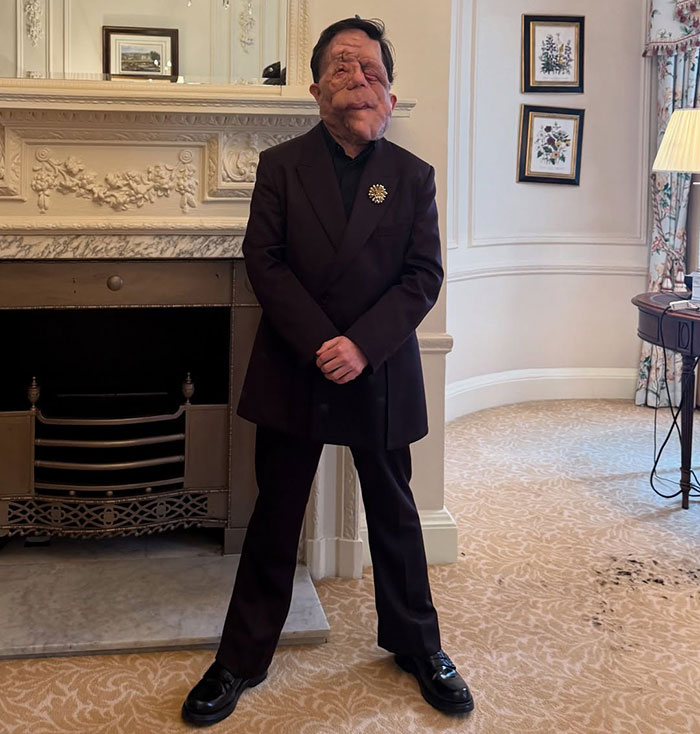 Person in a formal suit stands confidently by a fireplace, showcasing resilience against "anti-trans" claims.