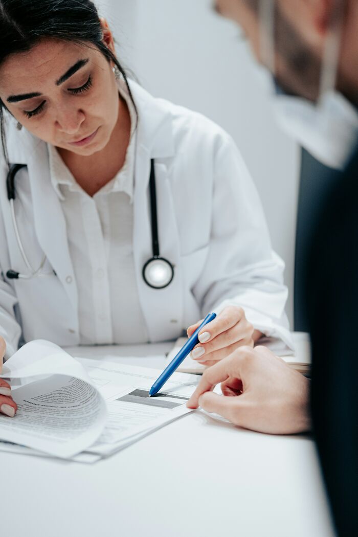 Doctor reviewing paperwork with a patient, highlighting challenges of adulthood with a pen.