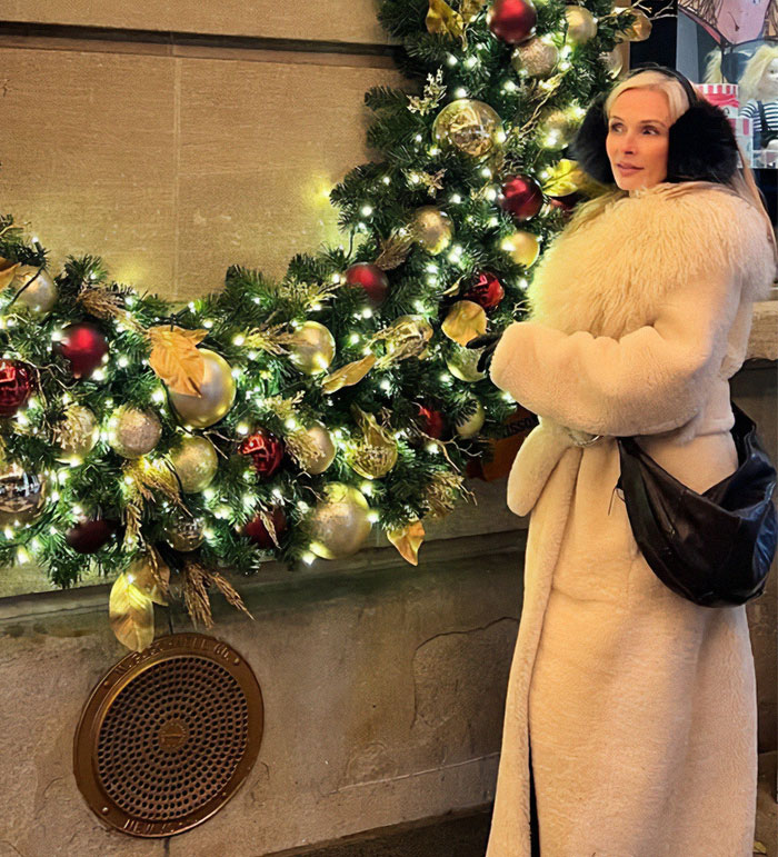Woman in a fur coat and earmuffs beside a decorated Christmas wreath, related to Bianca Censori controversy. Woman in a fur coat and earmuffs beside a decorated Christmas wreath, related to Bianca Censori controversy.