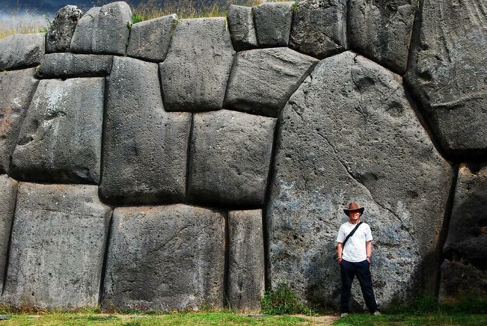 Person next to massive stone wall, showcasing artifacts from ancient civilizations.