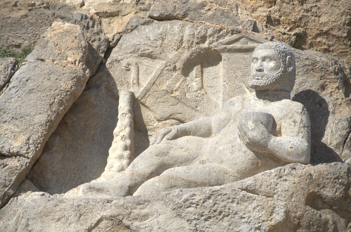 Ancient civilizations sculpture carved into rock, depicting a reclining figure holding an object, showcasing intricate details.