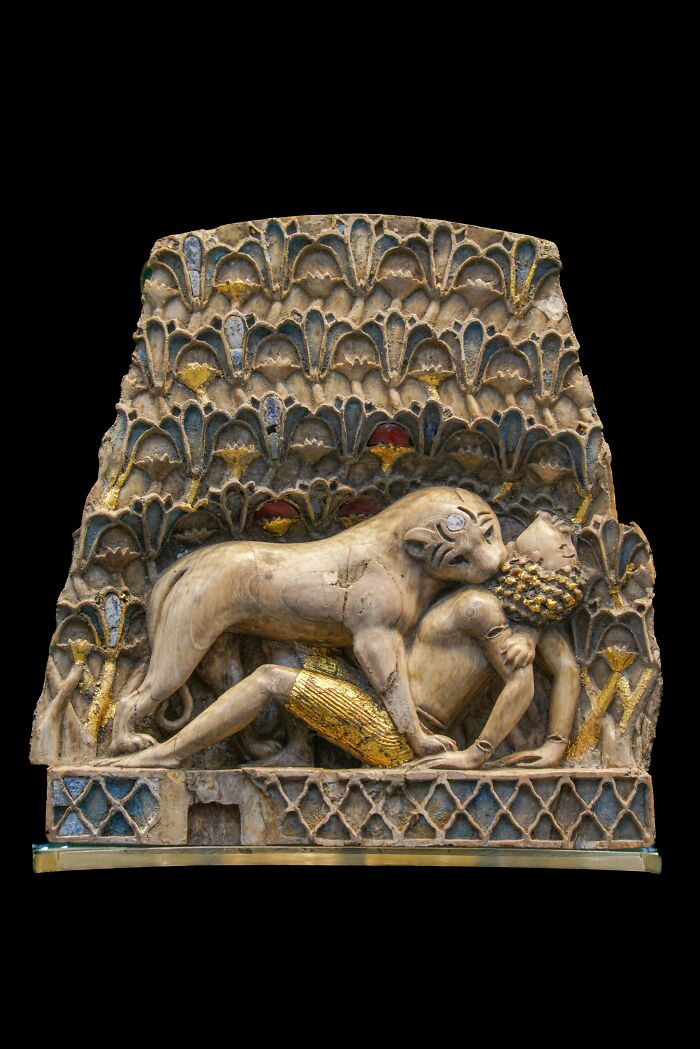 Ancient civilizations artifact depicting a lion attacking a human, with intricate decorative patterns in the background.