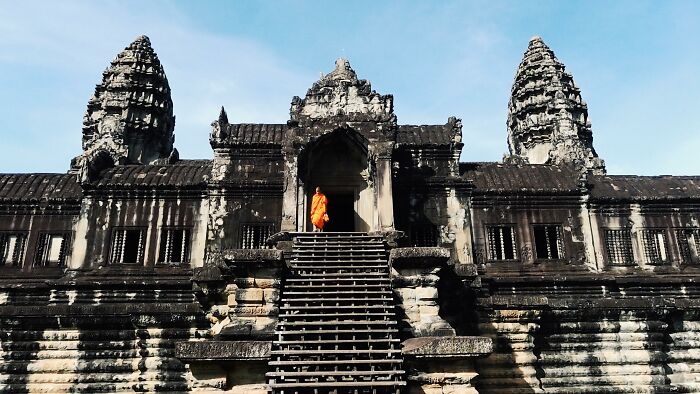 Monk in orange robe ascending steps of ancient civilization's temple at Angkor Wat.