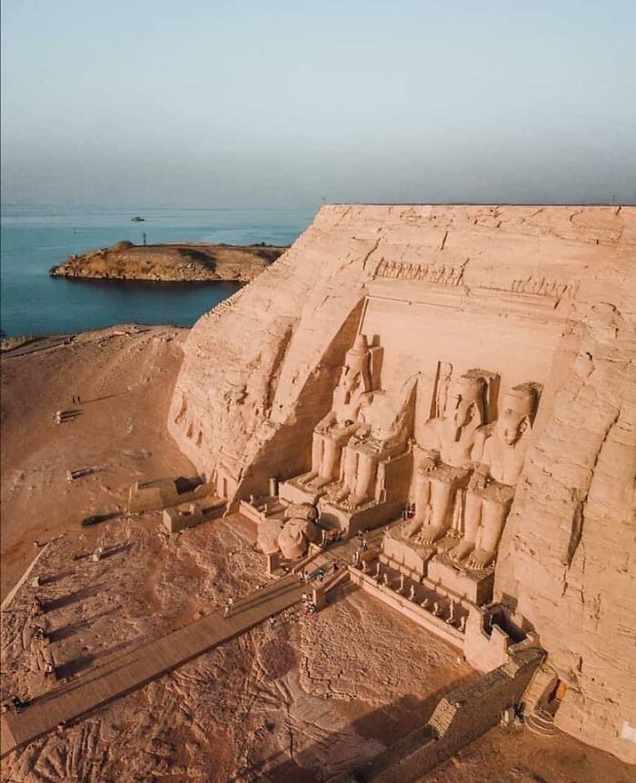 Ancient civilization artifacts: colossal statues at Abu Simbel, Egypt, near a serene body of water under a clear sky.