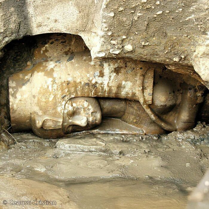Ancient statue partially buried in mud, showcasing artifacts from ancient civilizations.