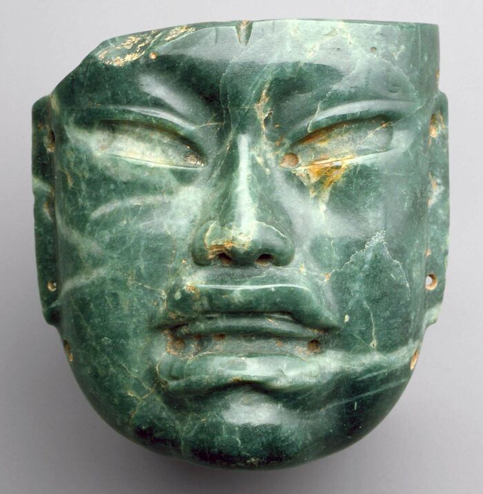 Ancient civilizations jade mask artifact, with intricate carvings and a smooth green surface.