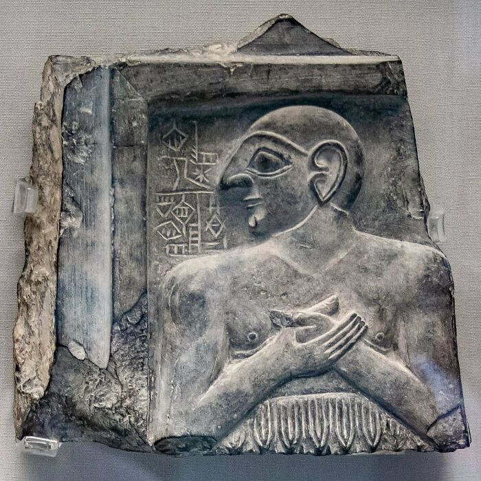 Ancient stone artifact depicting a sculpted human figure with intricate carvings and inscriptions.