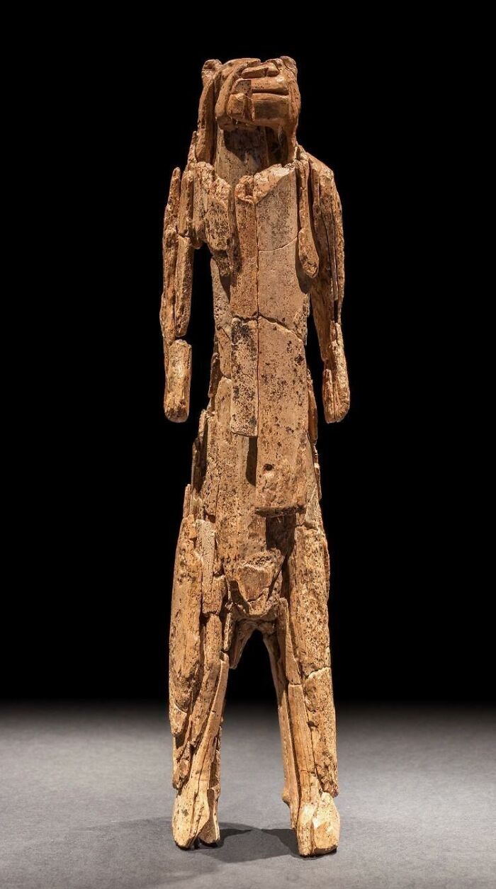 Ancient artifact sculpture resembling a humanoid figure on display against a dark background.