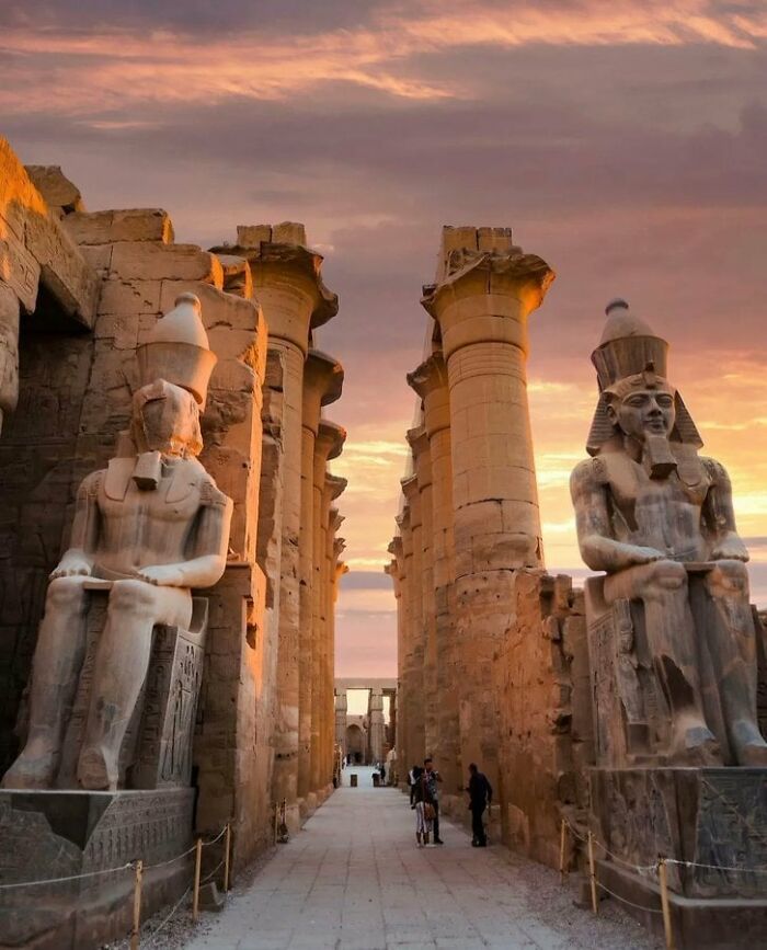 Ancient civilization artifacts at sunset with large statues and columns lining a stone pathway.