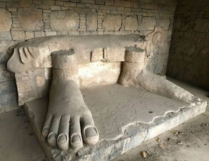 Ancient civilization artifact with large stone feet and brick wall background.